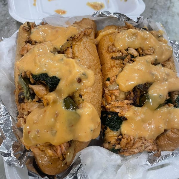 Two cheesy chicken cheesesteak sandwiches from Brunch Bro's 22nd St Cafe & Eatery, in a take-out container.