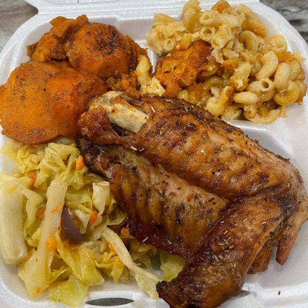 A soul food platter with baked chicken, macaroni and cheese, candied yams, and stewed cabbage.