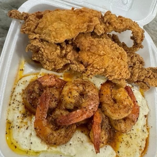 Fried chicken tenders and seasoned shrimp over grits in a white takeout container from Brunch Bro's.