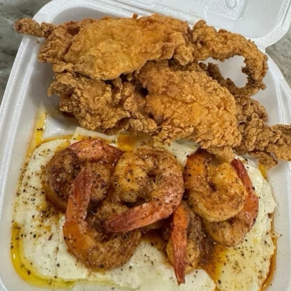 Fried chicken tenders and seasoned shrimp over grits in a white takeout container from Brunch Bro's.