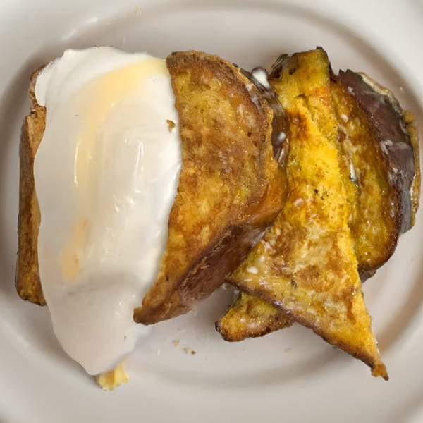 Golden-brown French toast slices, generously topped with a dollop of white cream and a drizzle of syrup.