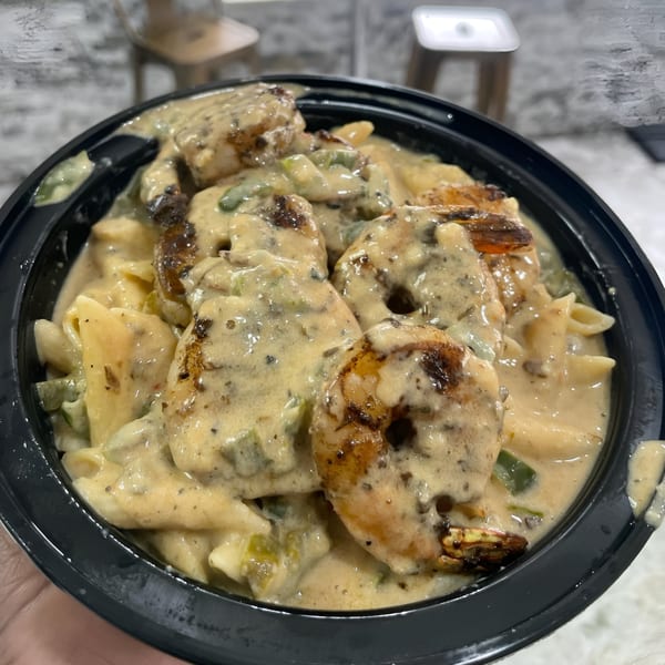 Creamy shrimp pasta with penne noodles and green peppers in a black bowl from Brunch Bro's.