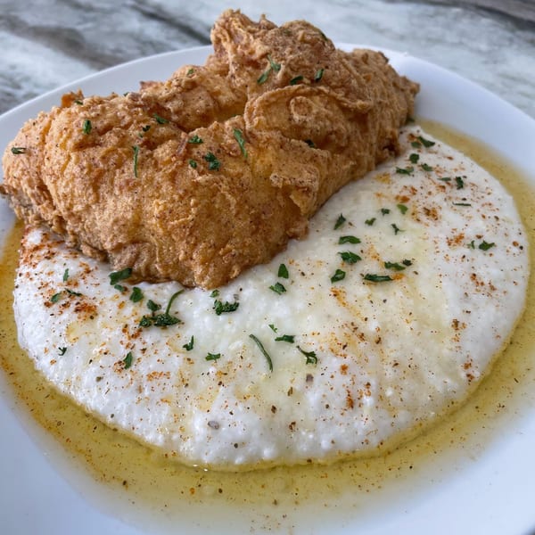 Golden fried chicken and creamy grits with herbs and spices on a white plate.