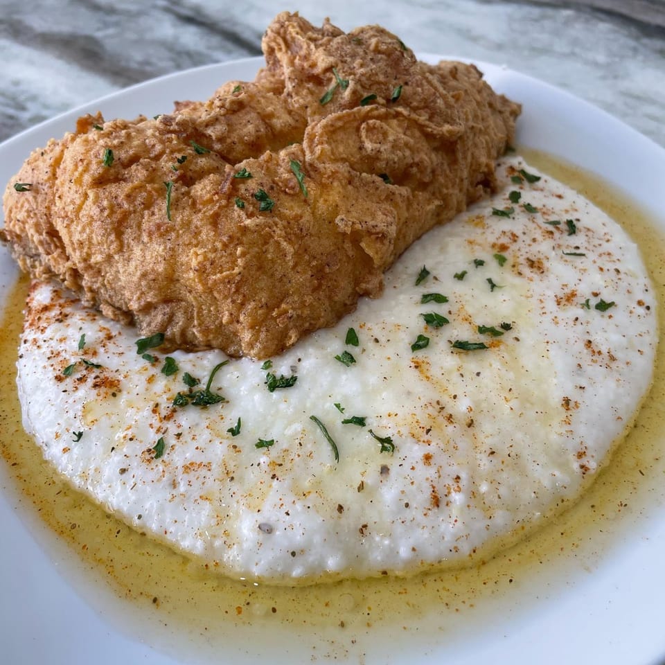 Golden fried chicken and creamy grits with herbs and spices on a white plate.